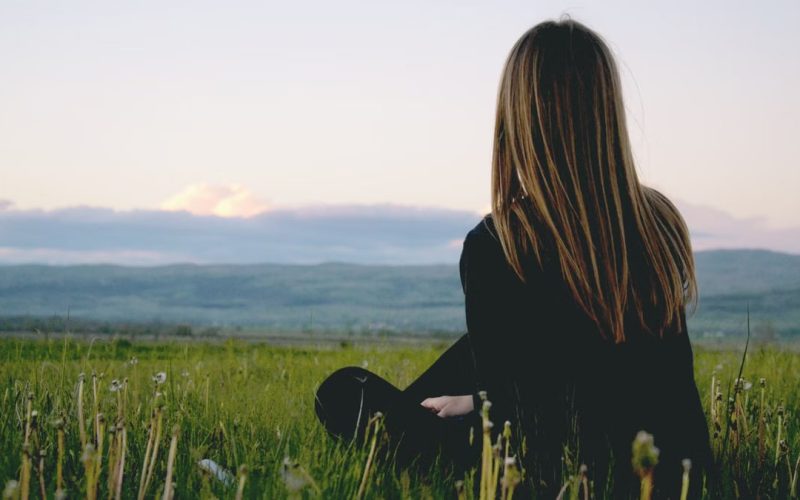 Woman enjoying peace in a lush green field with a scenic mountain view during sunset.